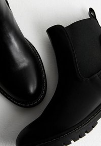 Czarne botki Chelsea wykonane z gładkiej skóry, z elastycznymi panelami po bokach oraz teksturowaną gumową podeszwą ozdobioną białymi przeszyciami.