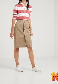 Beige knoopsluiting rok gemaakt van een katoenmix, met een zijsplit en een gladde textuur. Gecombineerd met een rood-wit gestreept shirt met lange mouwen en witte sneakers.