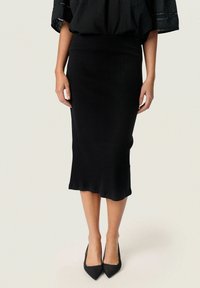Jupe midi noire en maille côtelée avec une silhouette ajustée, dotée d'un ourlet évasé. Associée à des talons noirs à bout pointu.