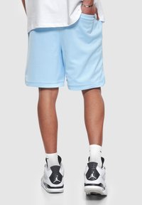 Shorts atléticos de malla azul con bolsillo, con un ajuste relajado. Combinados con zapatillas negras y blancas, que muestran un diseño y detalle clásico.
