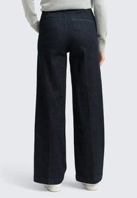 Pantalon large en denim foncé à taille haute, avec deux poches arrière et une texture lisse. L'ourlet est fini sans ornements.