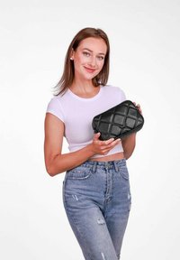 Černá prošívaná kabelka obdélníkového tvaru, s texturovaným povrchem a zipovým uzavíráním. Modelka drží kabelku a nosí bílé tričko.