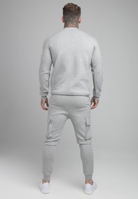 Sudadera de algodón gris con puños acanalados, combinada con pantalones cargo a juego que presentan bolsillos laterales y se estrechan en los tobillos, completada con zapatillas blancas.