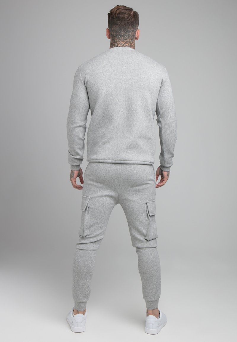 Sudadera de algodón gris con puños acanalados, combinada con pantalones cargo a juego que presentan bolsillos laterales y se estrechan en los tobillos, completada con zapatillas blancas.