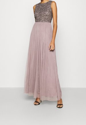 Woman wearing sleeveless gown with glittered fitted bodice and flowing pleated mauve skirt, paired with black high-heeled sandals.