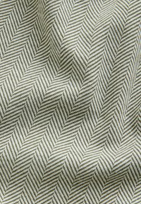 Detailný záber na textúrovanú tkaninu so šikmým vzorom rybej kosti v svetlosivých a bielych odtieňoch.