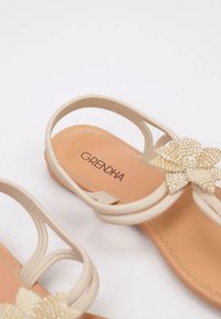 Sandalias beige con un acento floral texturizado, correas flexibles y una plantilla acolchada marrón con el nombre de la marca "GRENDHA."