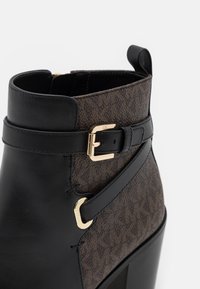 Bottine à cheville avec devant en cuir noir, dos en tissu marron à motif, détails de boucle et de sangle dorés, et talon haut épais.