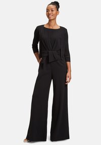 Fekete overál, derék résznél masni részlettel, rövid ujjú, textúrált, könnyű kardigán, széles lábakkal, sima szövetfelülettel.