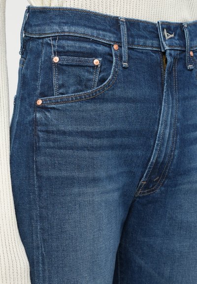 Denim jeans v temno modrem pranju, s bronastimi zakovicami, klasičnim dizajnom petih žepov in kontrastnimi podrobnostmi šivanja.