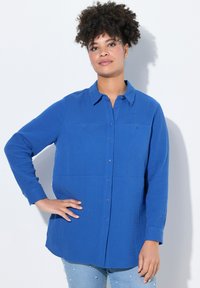 Camicia azzurra abbottonata realizzata in tessuto testurizzato con due tasche frontali. Maniche lunghe e colletto definito. Abbinata a jeans in denim chiaro.