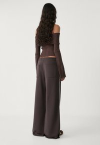 Off-shoulder ribbelbruine top gecombineerd met losse bruine sweatpants met twee achterzakken en een elastische tailleband.