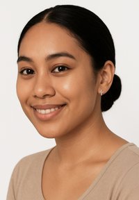 Orecchino a forma di croce argentata su un modello con capelli scuri, che indossa un top beige. Texture liscia, design minimalista e semplice dettaglio decorativo.