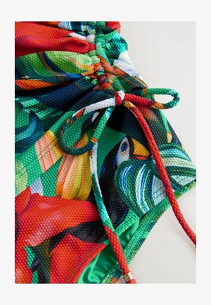 Kolorowy strój kąpielowy z żywym nadrukiem kwiatowym o teksturowanej powierzchni. Zapięcie na sznurek z czerwonymi akcentami i metalowymi detalami.