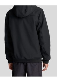 Sweatshirt à capuche noir avec une texture douce et lisse, présentant une coupe classique et des poignets côtelés, associé à un pantalon cargo sombre.