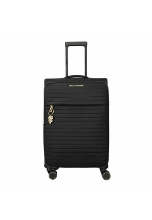 Maleta rígida negra con estrías horizontales, asa telescópica, bolsillo frontal con cremallera, cuatro ruedas y un charm dorado de flor en el tirador de la cremallera.