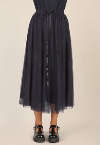 Falda midi de tul marina con cinturilla elástica y cinta de lazada. Combinada con zapatos negros de tacón grueso con detalles recortados.