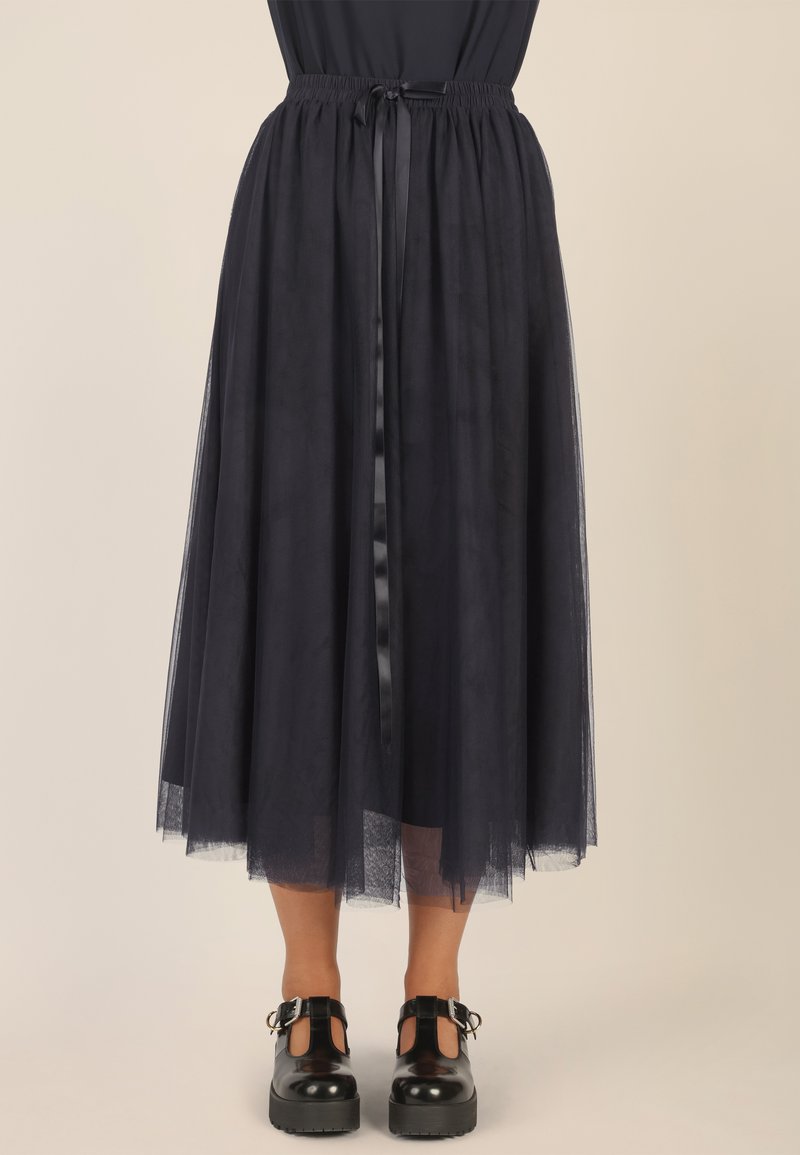 Falda midi de tul marina con cinturilla elástica y cinta de lazada. Combinada con zapatos negros de tacón grueso con detalles recortados.