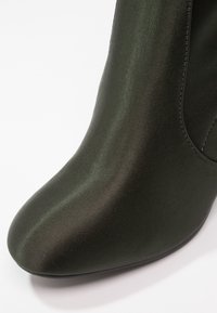 Bottine en satin vert foncé avec une finition lisse, un bout arrondi et un design sans couture avec des détails de couture subtils.