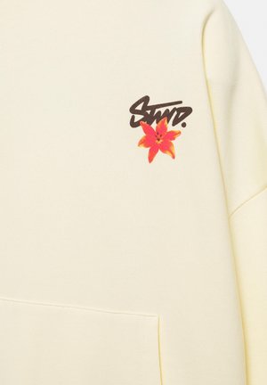 Sweat crème avec poche avant, texte noir stylisé "STWD." au-dessus d'une fleur rouge et orange en haut à gauche.