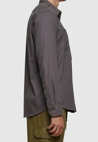 Szara koszula z długim rękawem z kołnierzykiem na guziki, kieszenią na piersi oraz regulowanymi mankietami. Wykonana z gładkiej tkaniny, o prostym kroju.