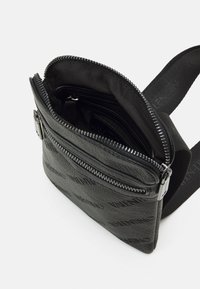 Černá kožená kabelka přes rameno s texturovaným povrchem a stříbrným zipem. Vnitřek obsahuje několik kapes pro organizaci. Nastavitelný popruh.