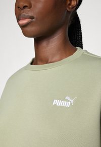 Felpa verde in misto cotone con maniche corte, colletto a costine e logo PUMA bianco sul lato sinistro del petto. Tessuto liscio, design informale.