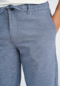 Jasnoniebieskie, teksturowane spodnie dresowe z elastycznym paskiem w talii, detalem w postaci sznurka oraz bocznymi kieszeniami. Materiał wydaje się być miękki i przewiewny.