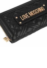 Portafoglio in pelle nera trapuntata con una placca dorata "LOVE MOSCHINO", accenti in metallo dorato e chiusura con zip.