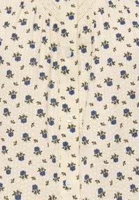 Υφασμάτινο σε κρεμ χρώμα με μικρό μπλε floral σχέδιο, υφασμένο με απαλές κουκκίδες, με κουμπιά μπροστά και λεπτή δαντέλα κοντά στη λαιμόκοψη.