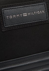 Sneaker in tessuto nero con un'etichetta in pelle nera in rilievo, caratterizzata da testo "TOMMY HILFIGER" in argento e bordi cuciti.