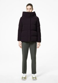 Giacca a vento di colore viola scuro con colletto alto, chiusura con bottoni e design trapuntato. Indossata con pantaloni verde oliva e sneakers bianco-verdi.