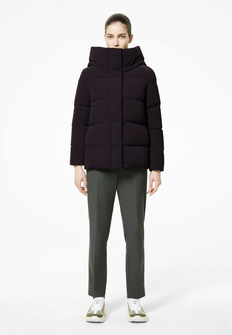 Giacca a vento di colore viola scuro con colletto alto, chiusura con bottoni e design trapuntato. Indossata con pantaloni verde oliva e sneakers bianco-verdi.