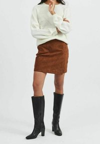 White knit sweater with textured pattern, brown suede skirt, and black knee-high heeled boots. Simple, modern style with clean lines.