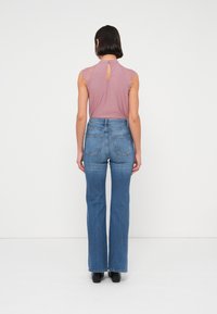 Απαλό ροζ μπλουζάκι χωρίς μανίκια με δαντελένιο τελείωμα στους ώμους και άνοιγμα στην πλάτη, σε συνδυασμό με ψηλόμεσα μπλε καμπάνα τζιν.