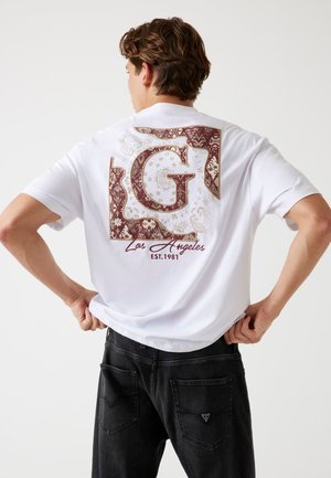 Camiseta blanca con un gran diseño gráfico en burdeos y dorado en la parte posterior, que incluye "G", "Los Ángeles" y "EST. 1981." Tejido texturizado.