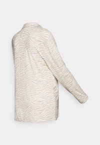 Beige jas met lange mouwen en een gestructureerd zebra patroon. Zacht materiaal, op maat gemaakte ontwerp, open voorkant en iets losser pasvorm.