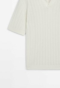 Pull en maille crème à manches courtes avec motif côtelé et petit col en V sur fond blanc.