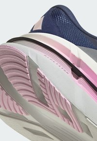 Chaussure de sport avec un dessus bleu marine et gris, des panneaux en maille texturée, et une semelle en caoutchouc rose et blanche avec un profil de bande de roulement à motifs.