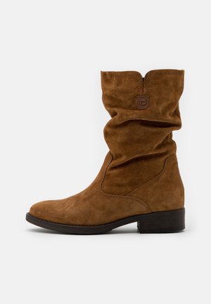 Bottine en daim marron avec un design décontracté, un bout rond et un petit talon empilé. Présente des détails cousus et une petite étiquette logo.