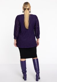 Paarse lace blouse met driekwart mouwen en knoopdetails, gecombineerd met een zwarte kokerrok en kniehoge paarse leren laarzen.