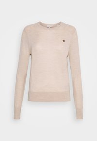 Pull en tricot beige clair avec des manches longues, un col rond et un petit logo brodé sur la poitrine. Texture lisse et design ajusté.