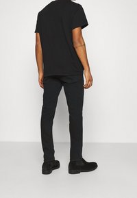 Svart bomullströja med korta ärmar, avslappnad passform, kombinerad med mörka jeans och svarta mocka stövletter, vilket visar en enkel, avslappnad stil.