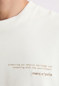 Biała bawełniana bluza z ribbowym okrągłym dekoltem oraz nadrukowanym brązowym tekstem: "zachowując nasze naturalne dziedzictwo" oraz "marc o'polo."