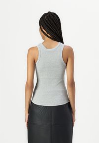 Siv tank top, prilegajoč v rebrasti tkanini, z zaobljenim ovratnikom in širokimi naramnicami, v kombinaciji s črno usnjeno krilom.