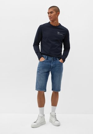 Navy long-sleeve shirt, light blue denim shorts, white sneakers, and white crew socks. Shorts have a straight cut, no visible patterns.