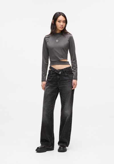 Crop top gris à manches longues avec un détail découpé circulaire et un jean large taille haute noir avec des coutures visibles et un accent en bouton.