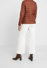 Brown quilted puffer jacket with a fitted design, paired with white wide-leg pants and brown heeled ankle boots, viewed from the back.