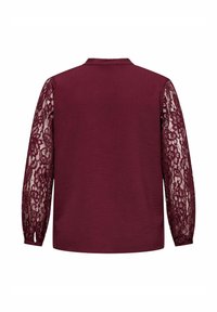 Top color bordeaux con corpo strutturato e maniche lunghe in pizzo, con colletto e vestibilità ampia. Il motivo in pizzo è floreale e intricato.