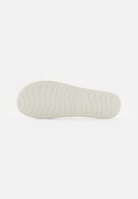 Weißer Gummi-Schuhsohle mit strukturiertem Muster, das wellenförmige Rillen und Markenlogo zeigt. Glatte Oberfläche mit leicht erhöhten Kanten.